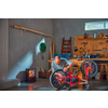 Man kneeling in a workshop repairing an upside-down red bicycle; workbench with tools, ladder, wood stove with visible flame, and a green hose on the wall