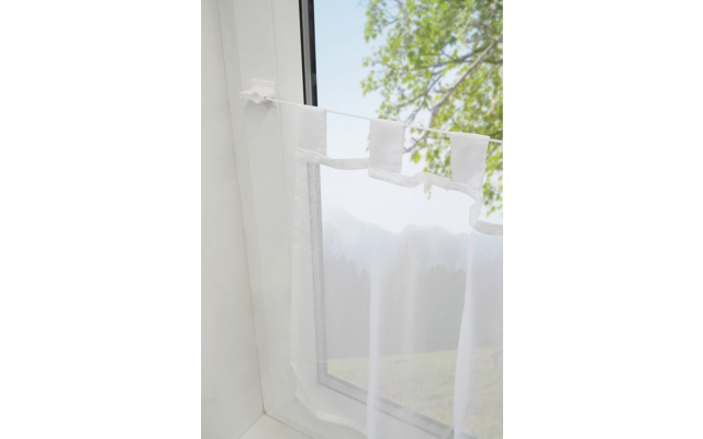 Weiße Gardine vor einem geöffneten Fenster mit Blick auf grüne Blätter