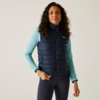 Vrouw met krullend haar draagt een blauw gestept vest en een lichtblauwe trui