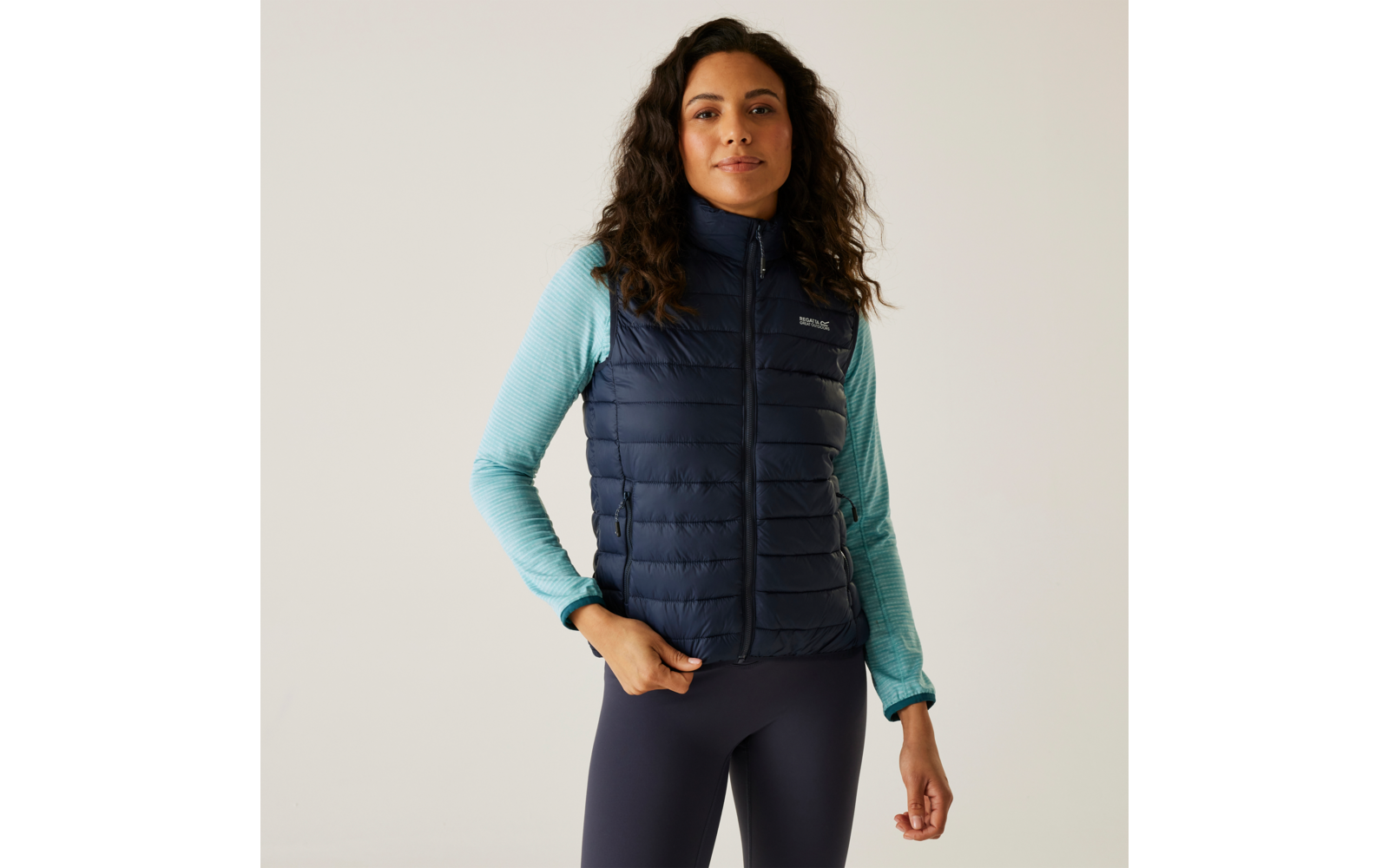 Vrouw met krullend haar draagt een blauw gestept vest en een lichtblauwe trui