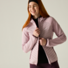 Smiling woman with red hair and headband closing a light pink quilted jacket over a black top against a light background