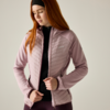 Person with long red hair and black headband fastening a light pink quilted jacket over a black zip-up top