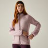 Person with long red hair and black headband wearing a light pink quilted zip-up jacket and dark leggings, one hand at hip, plain light background
