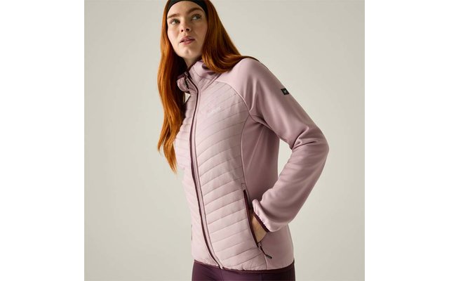 Person with long red hair and a black headband, wearing a light pink quilted zip jacket, hands in side pockets, light background