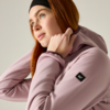 Person with red hair and headband wearing a pink hoodie, adjusting the hood, looking up-right against a light plain background