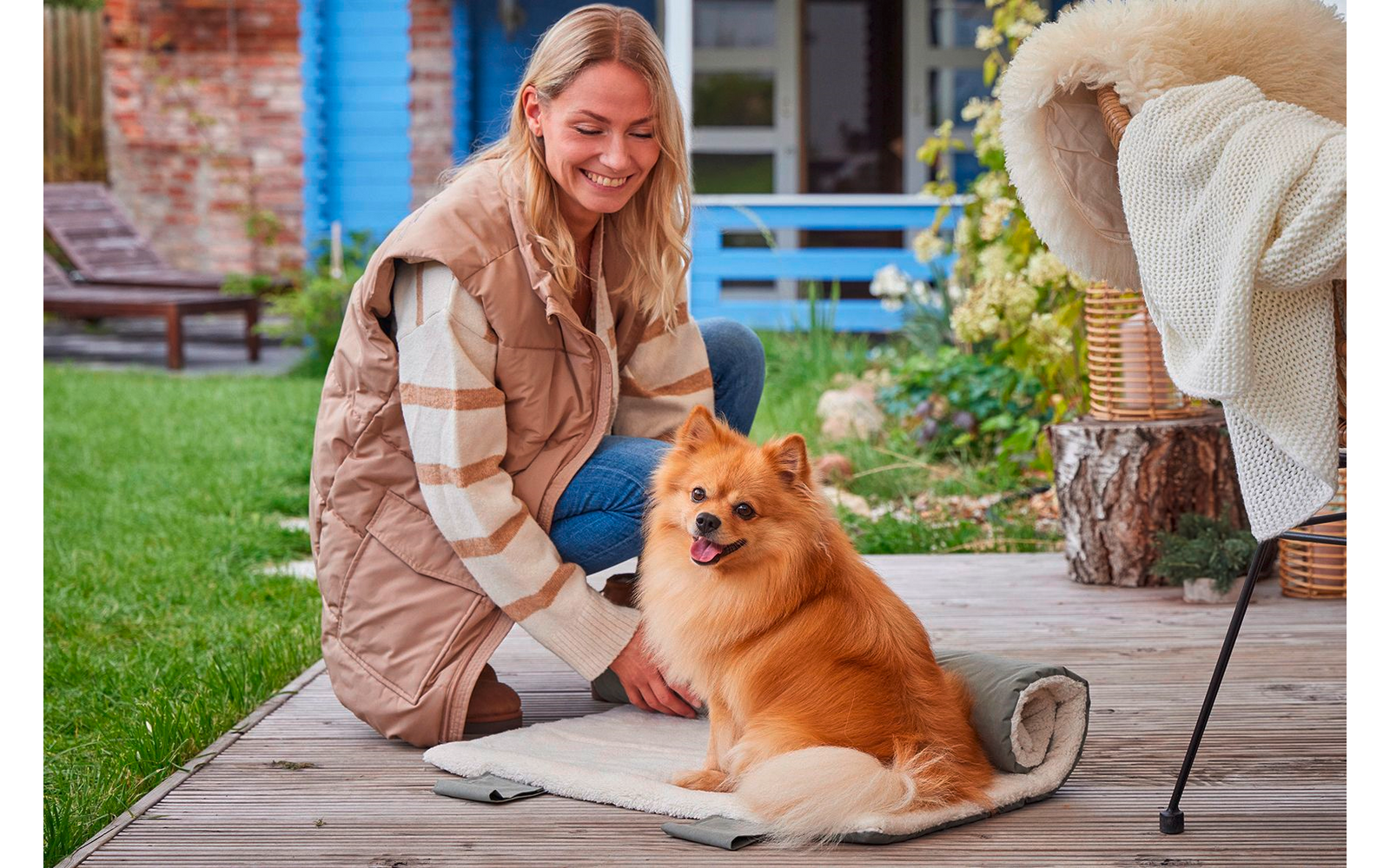 Frau kniet neben einem kleinen Hund im Garten und streichelt ihn