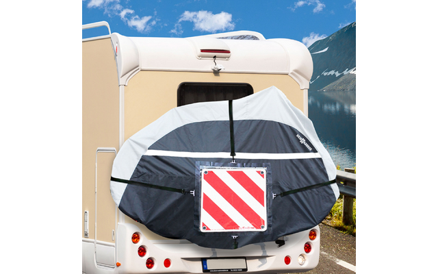 Vista posteriore di un camper chiaro con una ruota di scorta coperta da una copertura nera e grigio chiaro con una targa di segnalazione rossa e bianca a strisce diagonali; finestrino posteriore, fanali e targa visibili; lago, montagne e cielo azzurro con nuvole sullo sfondo