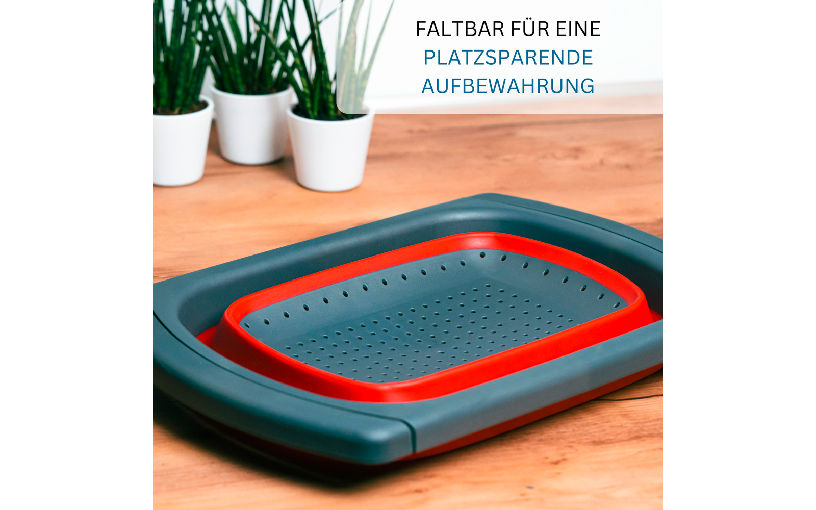 Passoire/égouttoir rectangulaire pliée gris et rouge sur un plan de travail en bois; trois petites plantes en pots blancs en arrière-plan; en haut à droite texte allemand : 'FALTBAR FÜR EINE PLATZSPARENDE AUFBEWAHRUNG'