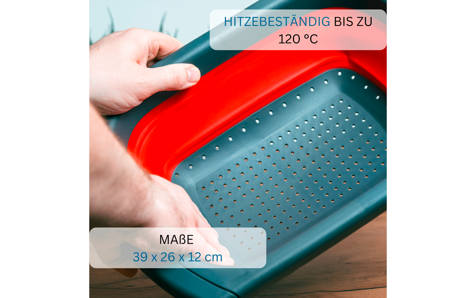 Deux mains tiennent une passoire rectangulaire à bord rouge et fond turquoise perforé ; inscriptions visibles : 'HITZEBESTÄNDIG BIS ZU 120 °C' et 'MAßE 39 x 26 x 12 cm'