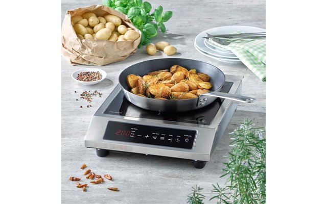 Koekenpan met aardappelpartjes op elektrische kookplaat, papieren zak met aardappelen, verse kruiden, borden en een kruidenkom op het aanrecht