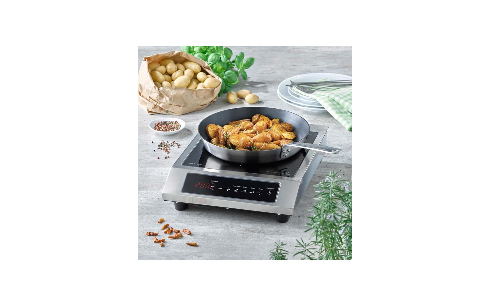 Koekenpan met aardappelpartjes op elektrische kookplaat, papieren zak met aardappelen, verse kruiden, borden en een kruidenkom op het aanrecht