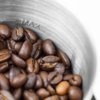 Braune Kaffeebohnen in einem Metallbehälter, im Inneren ist die Prägung "MAX" sichtbar