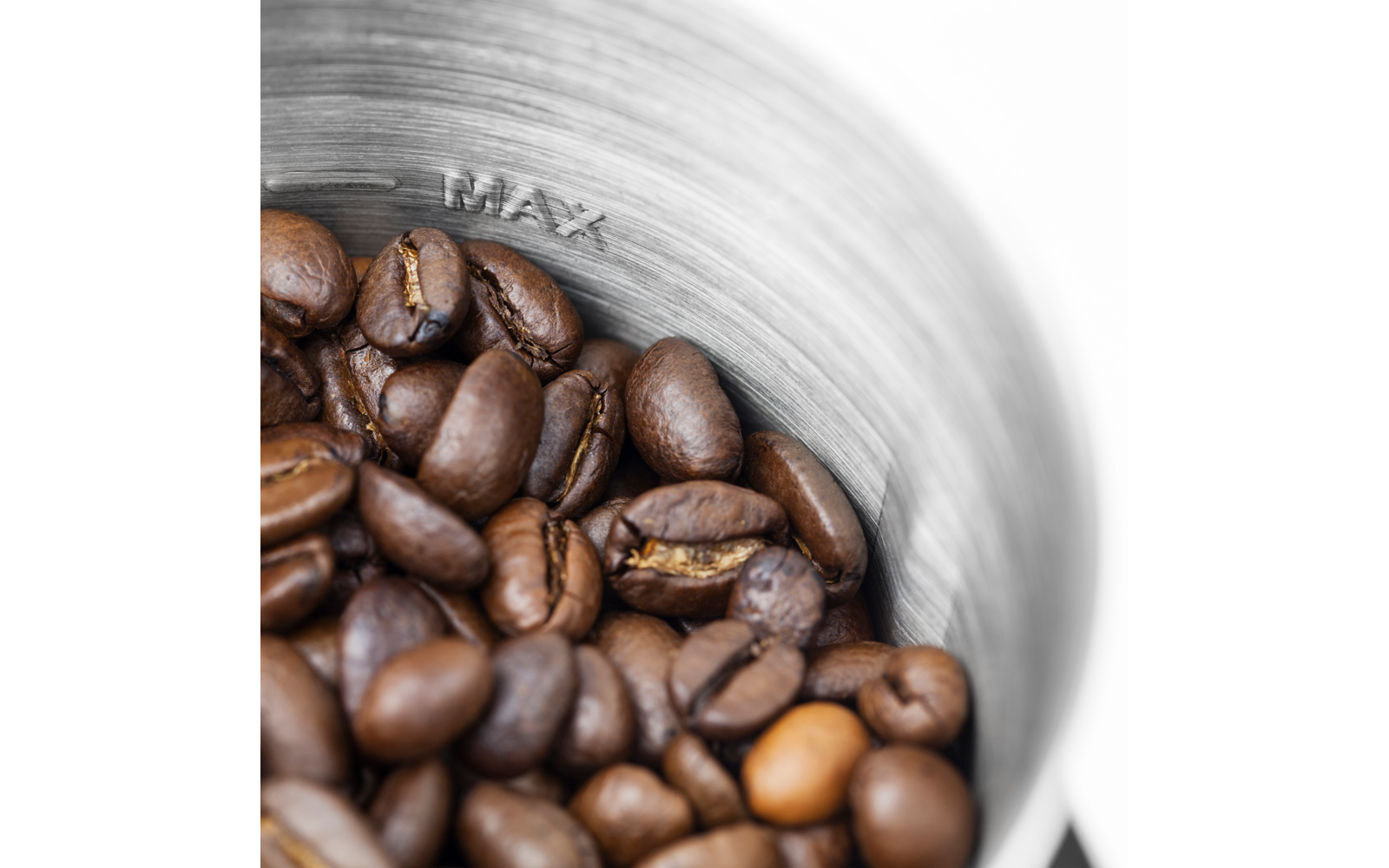 Braune Kaffeebohnen in einem Metallbehälter, im Inneren ist die Prägung "MAX" sichtbar