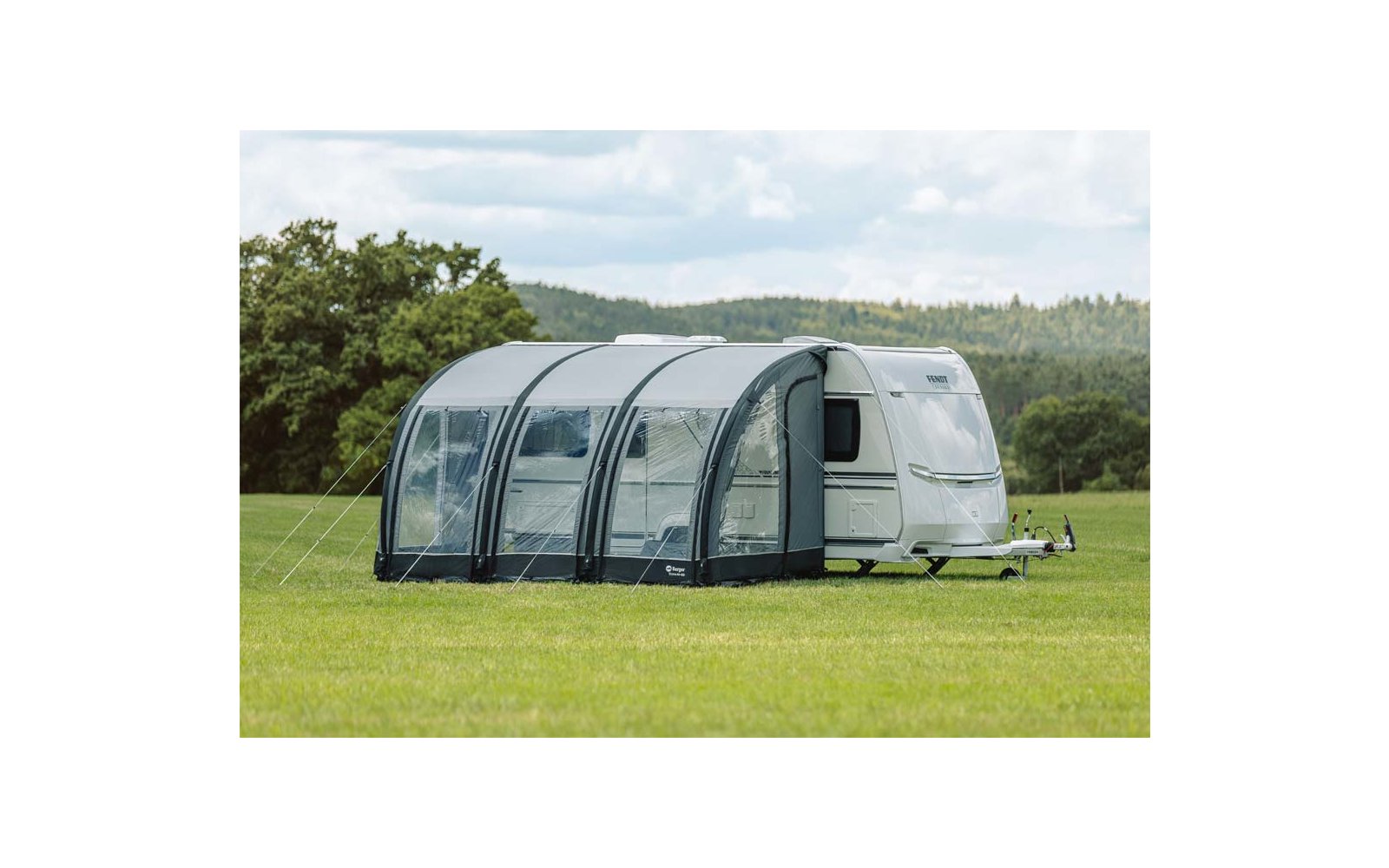 Weißer Wohnwagen mit grauem Vorzelt auf grüner Wiese unter blauem Himmel mit Wolken