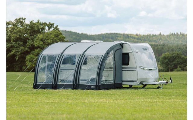 Weißer Wohnwagen mit grauem Vorzelt auf grüner Wiese unter blauem Himmel mit Wolken