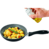 Hand hält ein kleines Glasfläschchen mit gelber Flüssigkeit über eine Pfanne mit goldbraunen kleinen Kartoffeln und einem Rosmarinzweig auf weißem Hintergrund