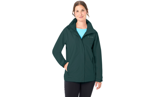 Person steht vor weißem Hintergrund, trägt dunkelgrüne Kapuzenjacke, hellblaues Oberteil, schwarze Hose, eine Hand in der Jackentasche