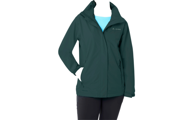 Persona de pie sobre fondo blanco que lleva una chaqueta con capucha verde oscuro, una prenda superior azul claro, pantalones negros, una mano en el bolsillo de la chaqueta