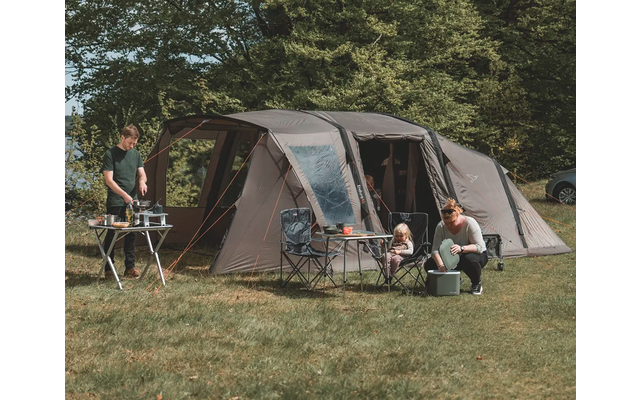 Großes graues Zelt auf einer Wiese mit vier Personen, Bäumen im Hintergrund
