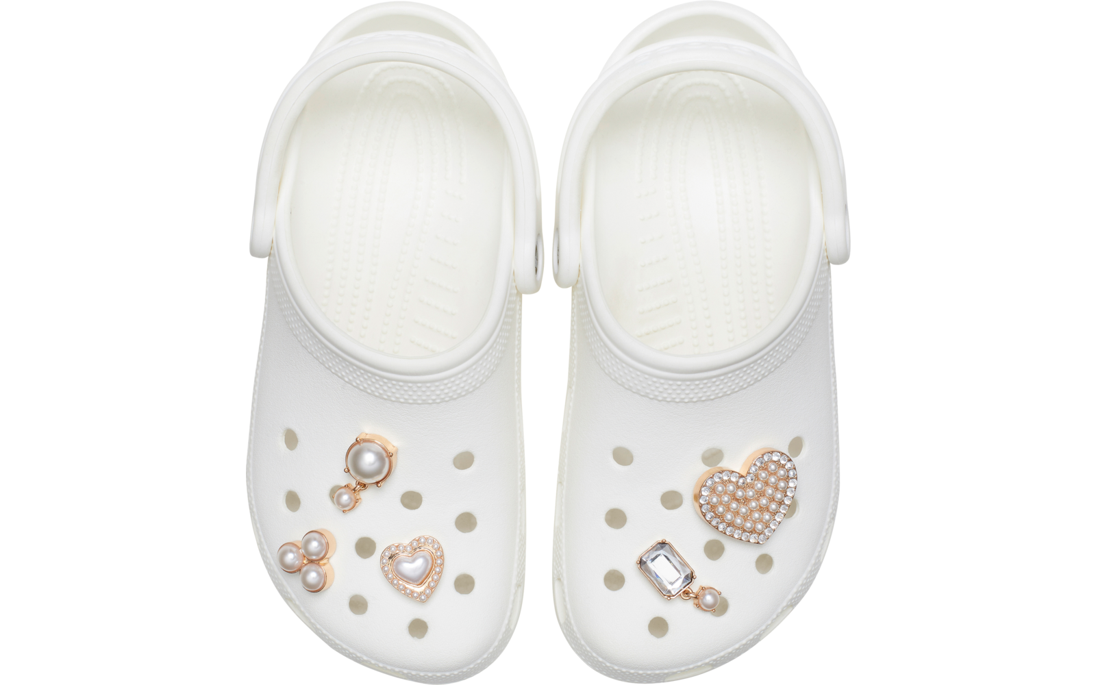 Deux sabots blancs avec des trous, décorés de breloques : perles, un cœur en strass et une pierre rectangulaire, vue de dessus