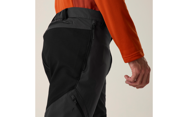 Gedeeltelijke weergave van een persoon van heup tot hand, oranje mouw, zwart-grijze broek met ritszakken