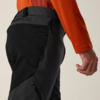Gedeeltelijke weergave van een persoon van heup tot hand, oranje mouw, zwart-grijze broek met ritszakken