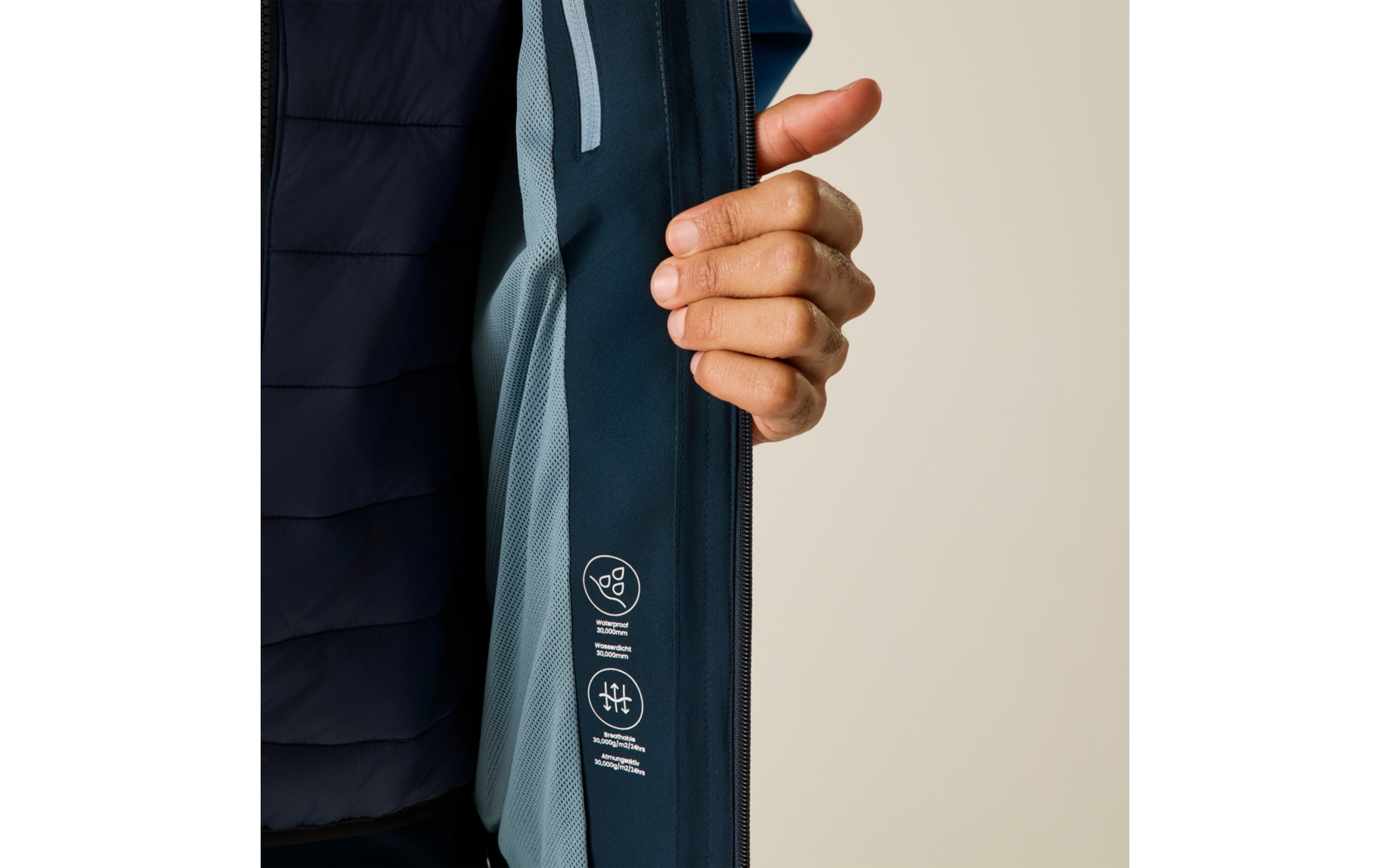 Hand öffnet Innenklappe einer dunkelblauen Jacke, sichtbar hellblaues Netzfutter und weiße Symbole/Textaufdrucke auf dem Innenbesatz