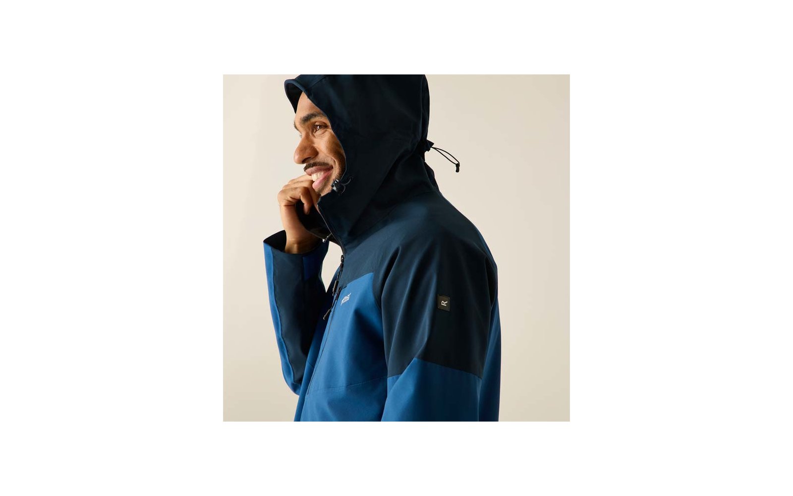 Person im Seitenprofil, lächelnd, trägt eine zweifarbige Kapuzenjacke und fasst die Kapuze mit einer Hand