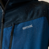 Nahaufnahme des oberen Teils einer blau-schwarzen Jacke mit Wasserperlen, zwei Reißverschlüssen und dem Schriftzug 'Regatta Great Outdoors'