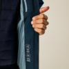 Hand öffnet Innenklappe einer dunkelblauen Jacke, sichtbar hellblaues Netzfutter und weiße Symbole/Textaufdrucke auf dem Innenbesatz