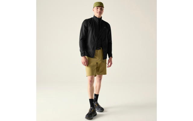Mann steht, trägt grüne Kappe, schwarze Jacke, khakifarbene Shorts, schwarze Socken und schwarze Sneaker, heller Hintergrund