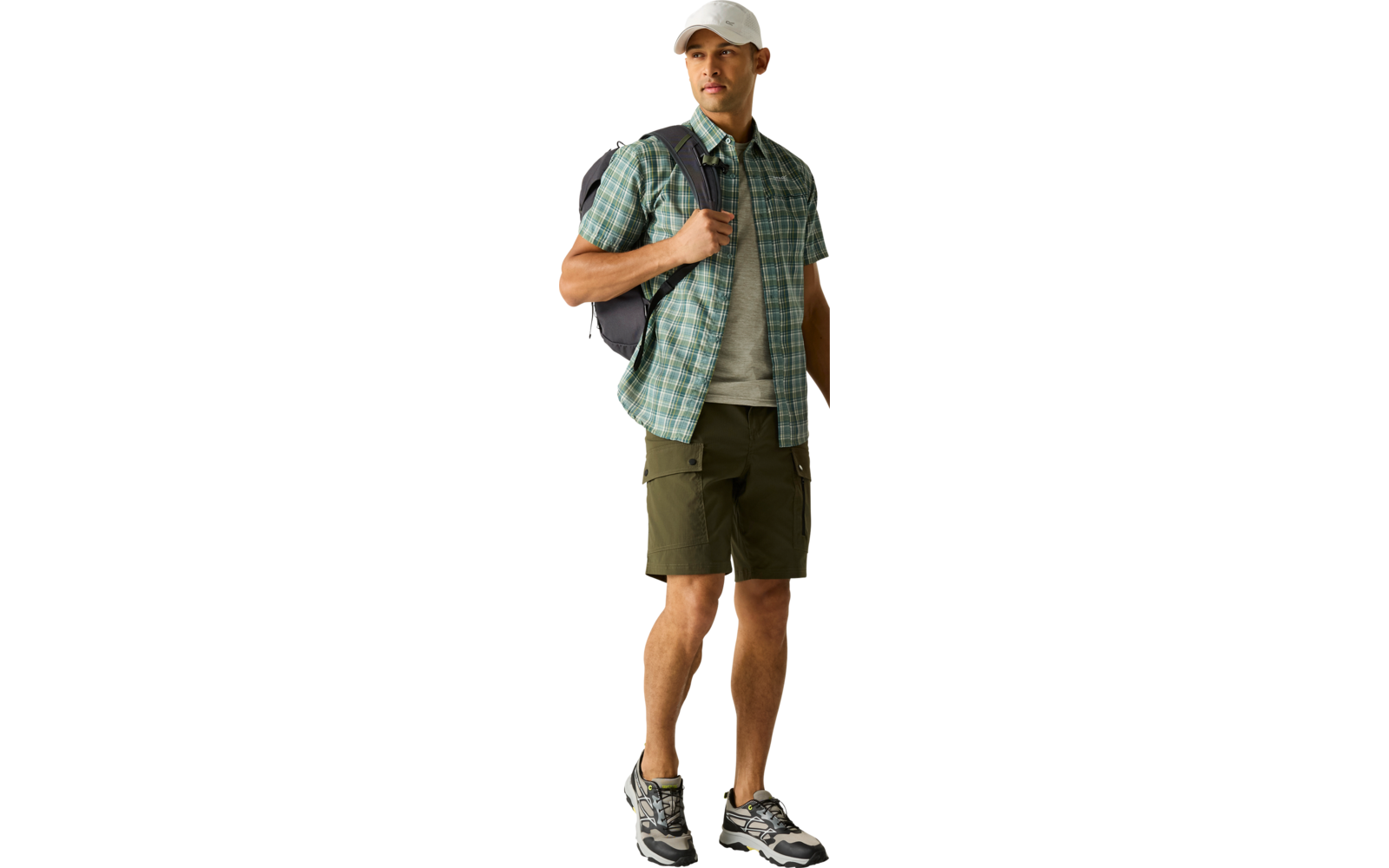 Stehende Person mit weißer Kappe, grün kariertem Hemd, grauem T‑Shirt, olivgrünen Shorts, Rucksack und Sneakers, Blick nach rechts