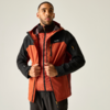 Mann vor hellem Hintergrund, trägt orange-schwarze Outdoorjacke über roter gesteppter Weste, hält Vorderseite der Jacke mit beiden Händen