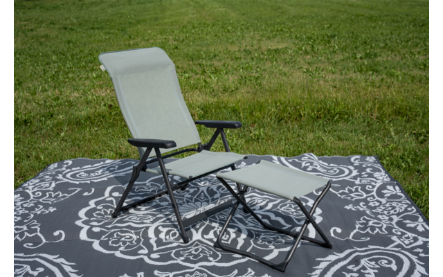 Fauteuil-longue pliant vert clair avec structure métallique noire et repose-pieds assorti sur un tapis gris foncé à motifs sur l'herbe