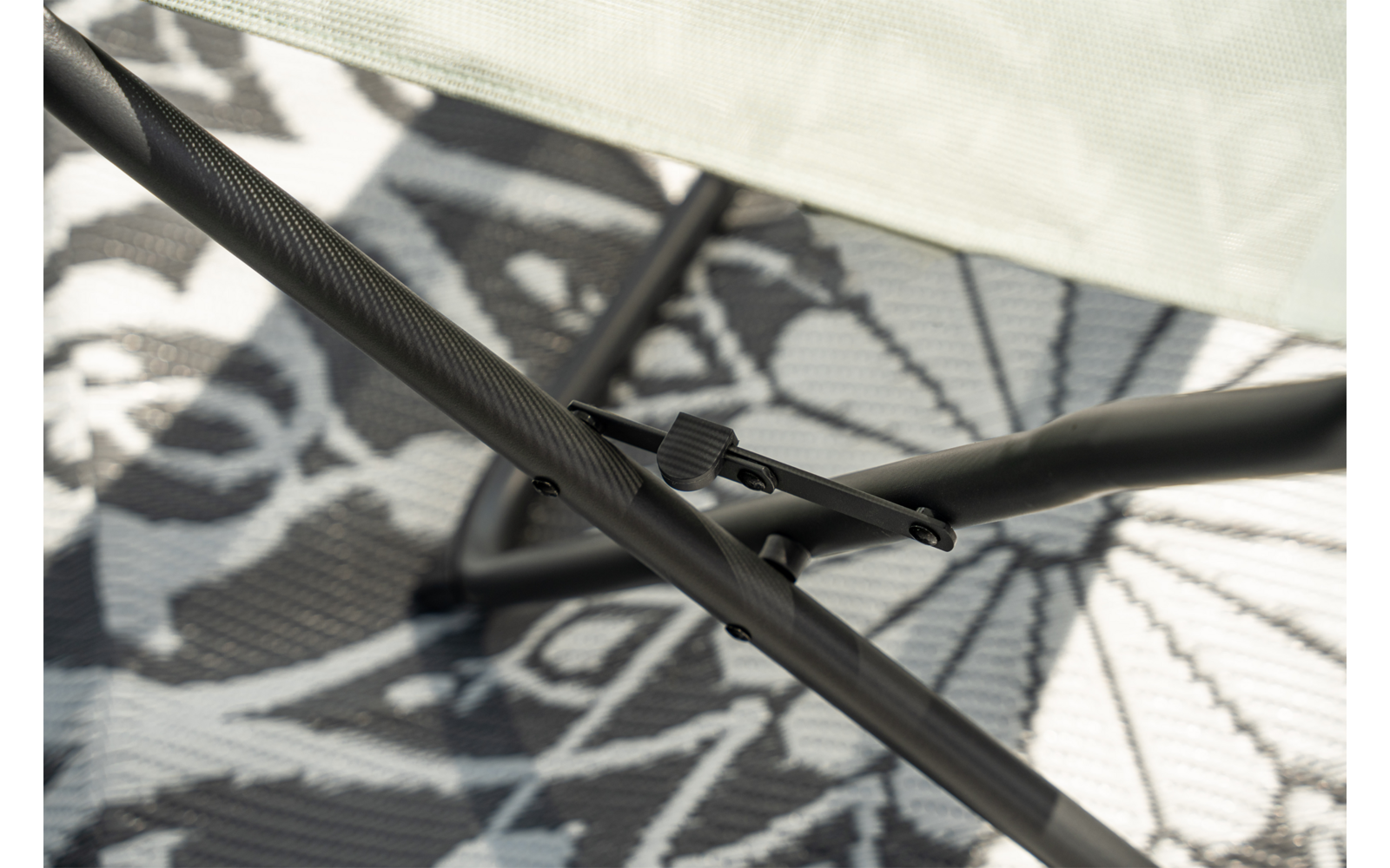 Tiges métalliques noires croisées avec vis et pince, au-dessus tissu en maille beige, en arrière-plan tapis au motif floral
