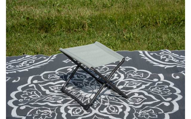 Petit tabouret pliant sur une couverture gris foncé à motif floral blanc, herbe en arrière-plan