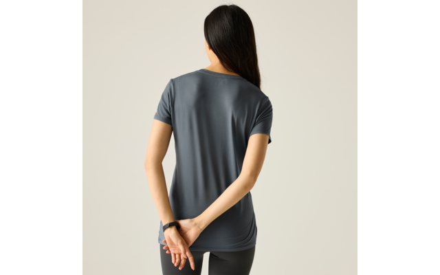 Rückansicht einer Person mit langen dunklen Haaren, graublauem T‑Shirt mit kurzen Ärmeln und schwarzen Leggings, Hände hinter dem Rücken verschränkt, heller einfarbiger Hintergrund