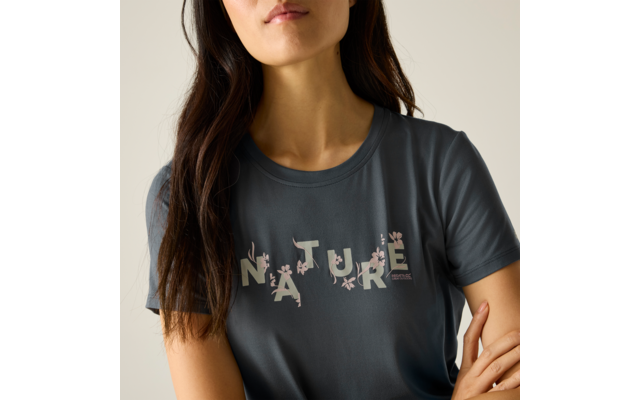 Oberkörper einer Person mit langen dunklen Haaren, sichtbares Kinn und Mund, graues T-Shirt mit dem Schriftzug "NATURE" und kleinen Blumenmotiven, Arme vor dem Oberkörper verschränkt