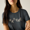 Oberkörper einer Person mit langen dunklen Haaren, sichtbares Kinn und Mund, graues T-Shirt mit dem Schriftzug "NATURE" und kleinen Blumenmotiven, Arme vor dem Oberkörper verschränkt