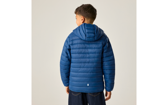 Junge steht mit dem Rücken zur Kamera, trägt eine blaue gesteppte Kapuzenjacke und dunkle Jeans vor hellem Hintergrund