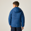 Junge steht mit dem Rücken zur Kamera, trägt eine blaue gesteppte Kapuzenjacke und dunkle Jeans vor hellem Hintergrund