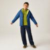 Lächelnder Junge steht mit leicht gespreizten Armen, trägt blaue Steppjacke, grüne Kapuzenjacke, dunkle Jeans und Sneakers vor neutralem Hintergrund
