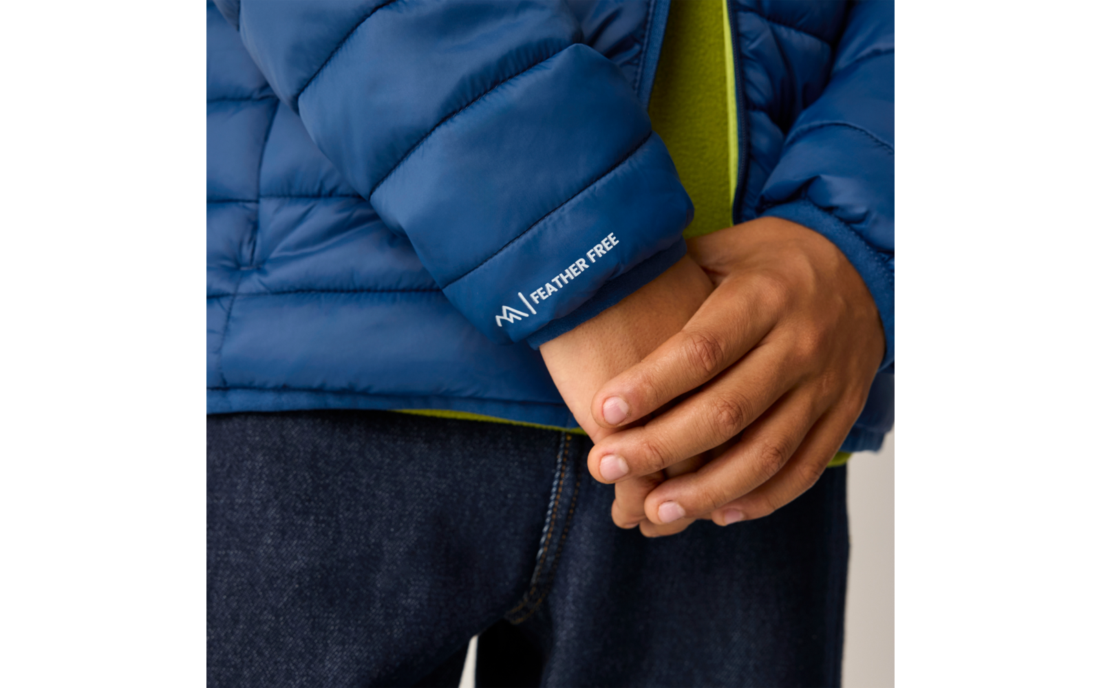 Nahaufnahme ineinandergreifender Hände vor dem Ärmel einer blauen Steppjacke mit dem Schriftzug 'FEATHER FREE', grüner Innenlage und dunkler Jeans