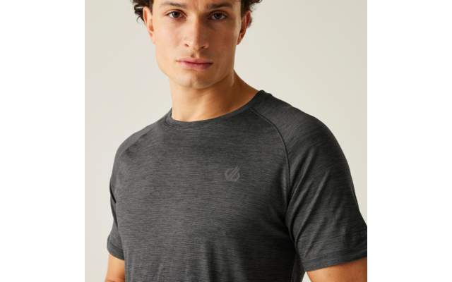 Gros plan d'une personne portant un T-shirt gris foncé à manches courtes, regardant la caméra, sur un fond uni clair