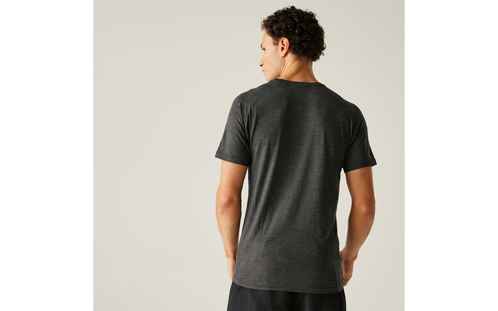 Personne vue de dos portant un t-shirt gris et un short noir sur un fond clair