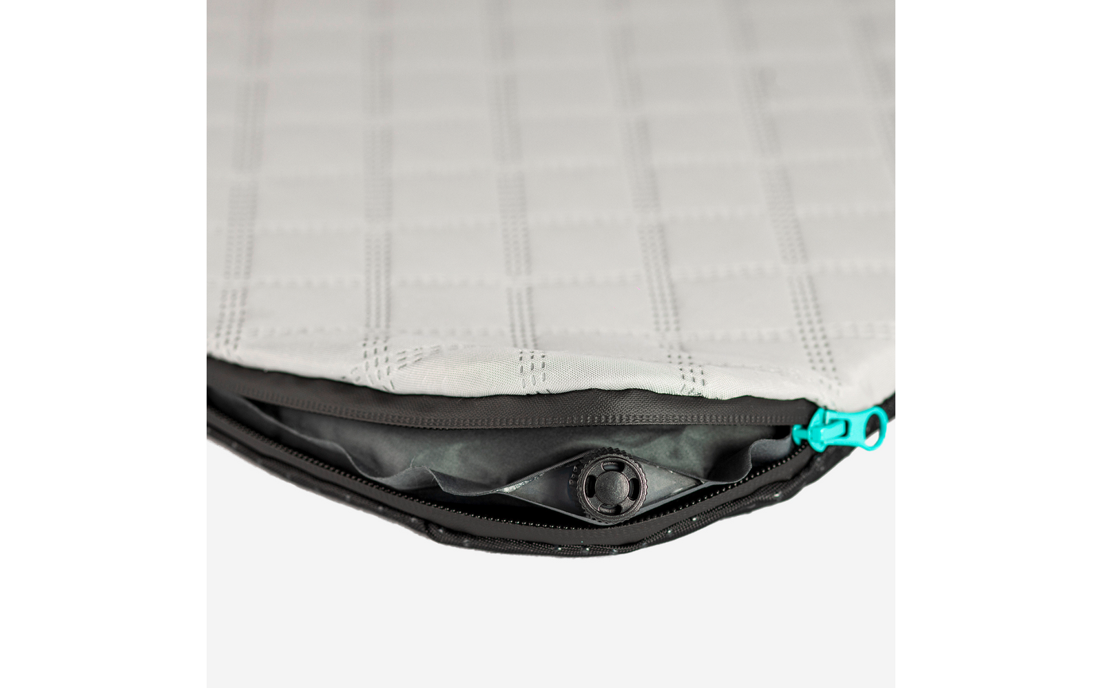 Offener Reißverschluss an grauem, gestepptem Stoff, sichtbar ist ein schwarzes Kunststoffventil und ein türkiser Reißverschlussanhänger