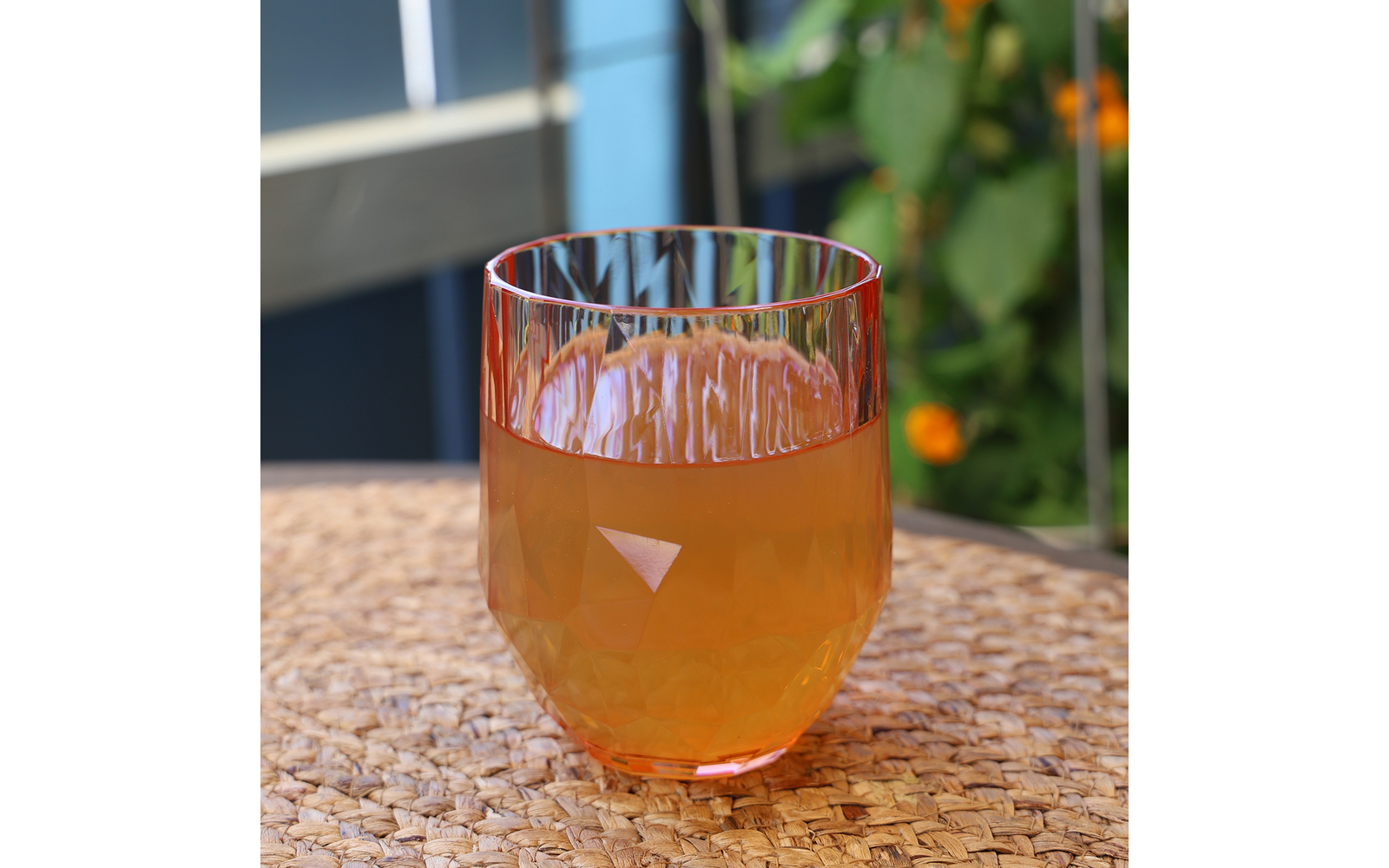 Ein transparentes Glas mit orangefarbenem Getränk, auf einem Mosaiktisch, im Hintergrund grüne Pflanzen