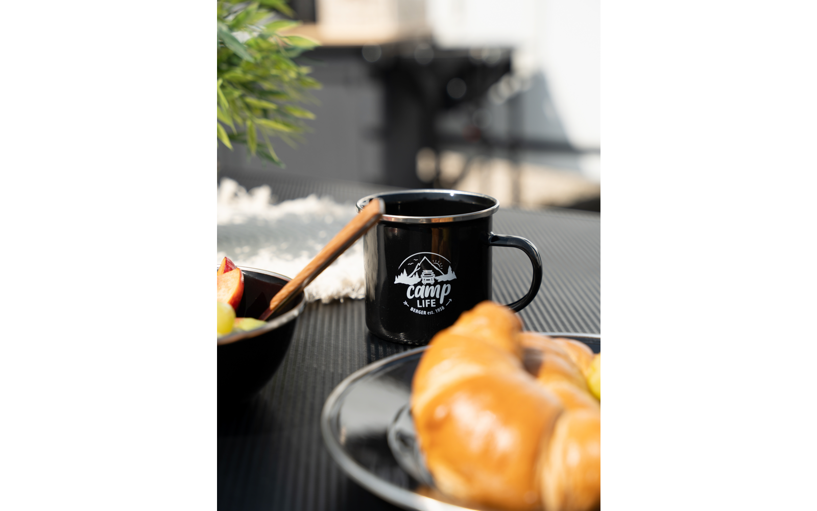 Tasse noire avec inscription sur une table, à côté d'une assiette avec des croissants