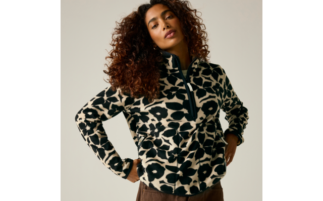 Personne aux cheveux bouclés portant un pull polaire noir et blanc à motif avec fermeture éclair, mains sur les hanches