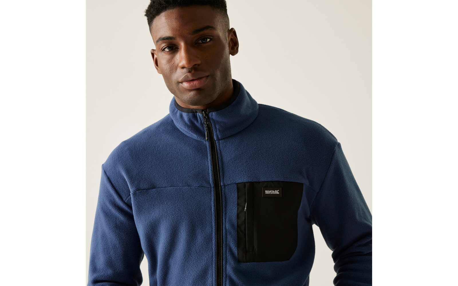 Junger Mann mit blauem Pullover und schwarzer Brusttasche vor hellem Hintergrund